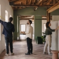Tres personas miden y observan la luz de una oficina vacía antes de elegir el espacio.
